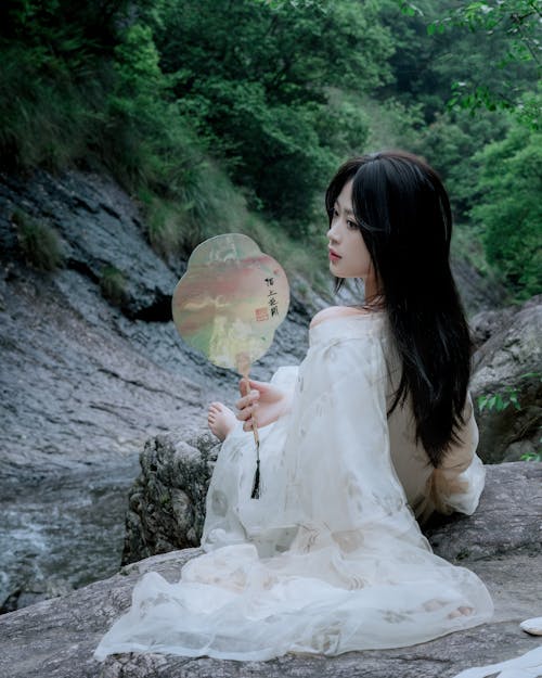 A woman sitting on a rock with a fan