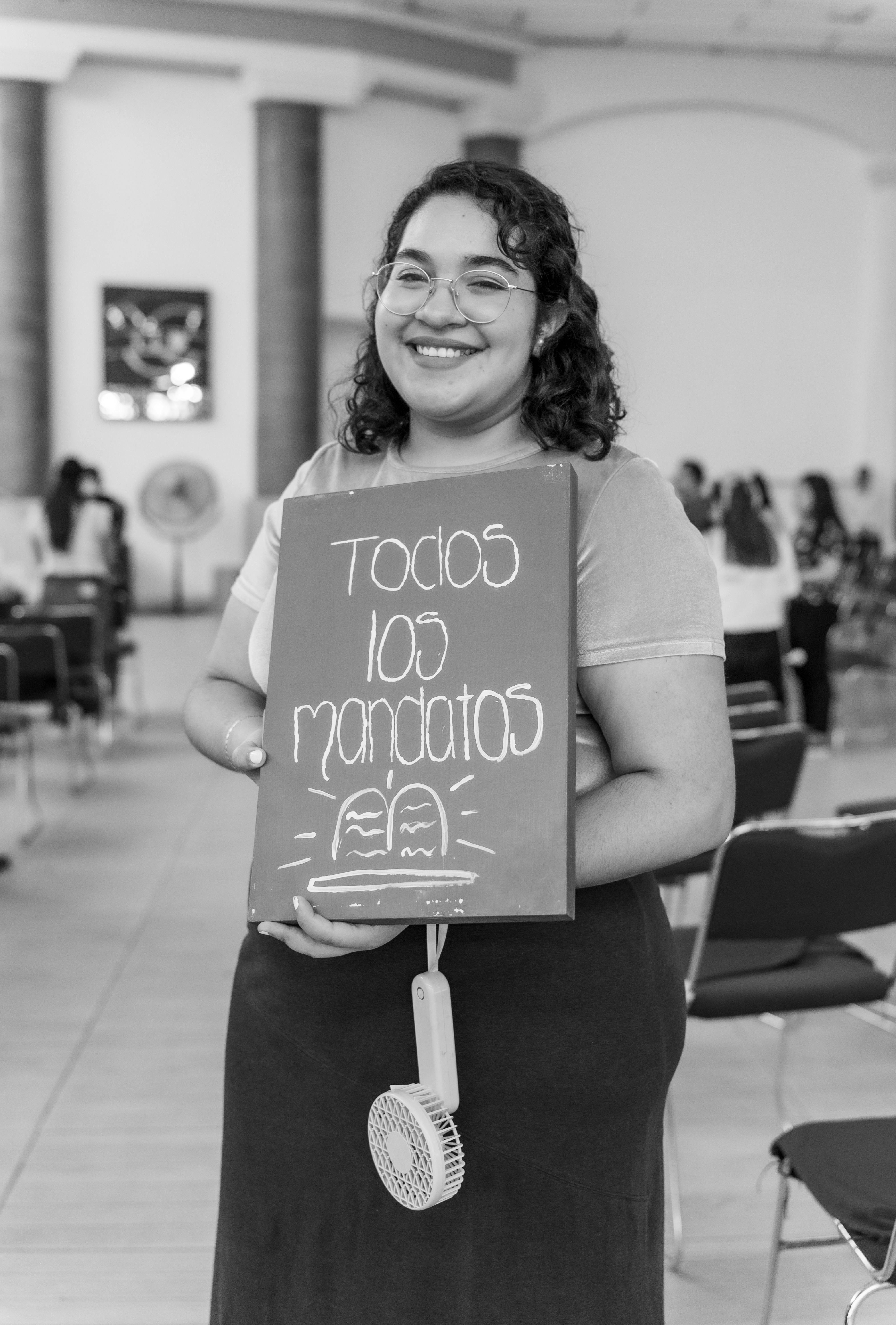 A woman holds a religious sign inside a church, smiling warmly at the camera.