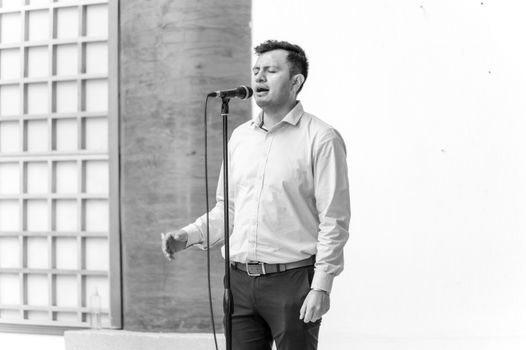 A man sings passionately into a microphone, captured in black and white, evoking a dramatic and classic feel.