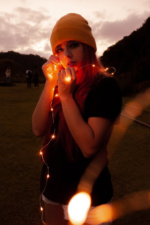 Free Woman in Black Shirt and White Shorts Holding Lighted String Light Stock Photo