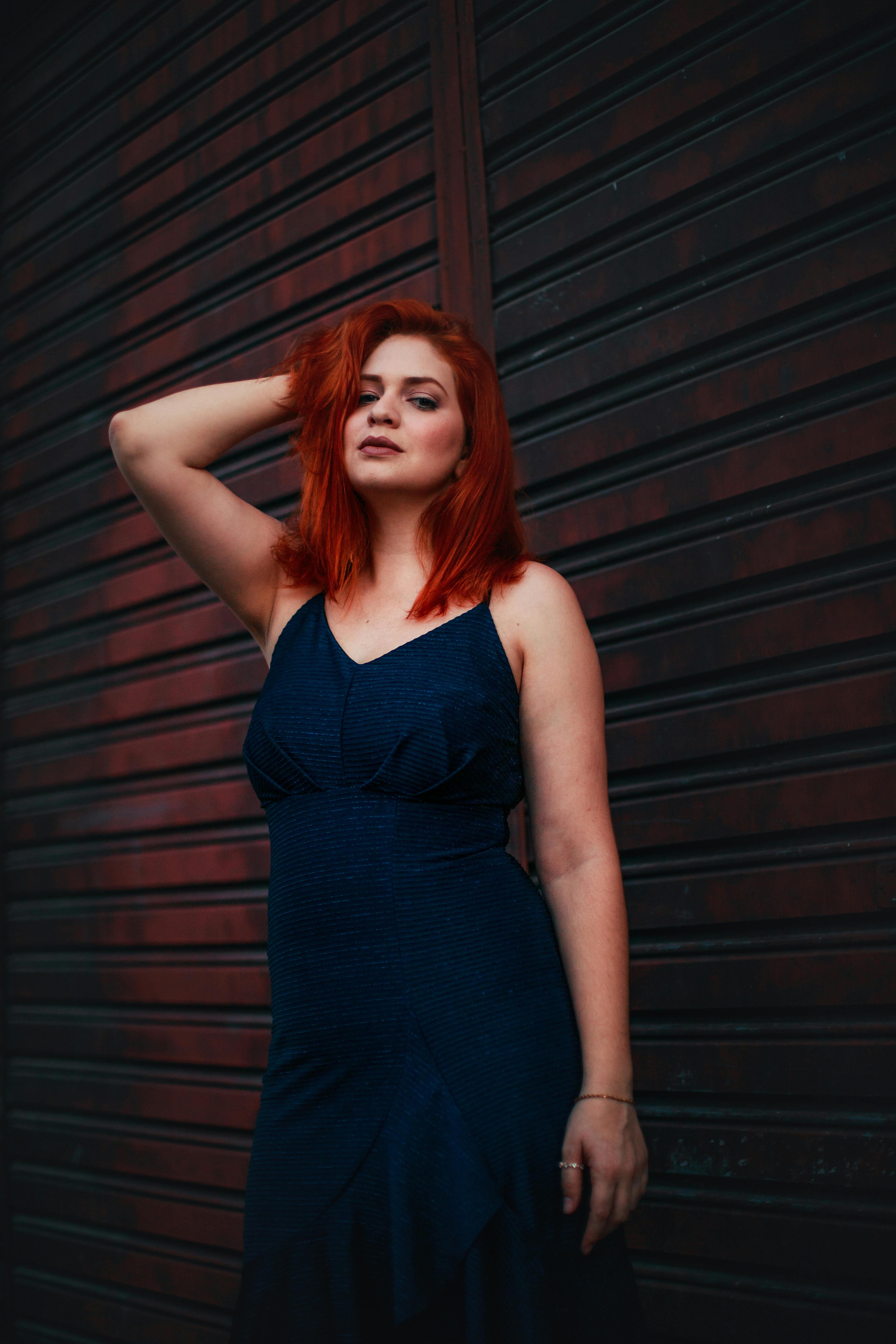 深色背景下，一位红发女子身着时尚的蓝色连衣裙