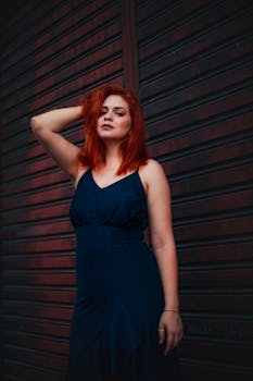 深色背景下，一位红发女子身着时尚的蓝色连衣裙
