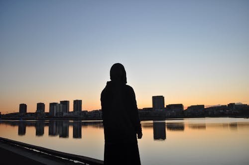 Silhouette of Standing Person Facing A Body of Water 