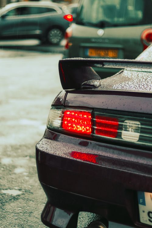 Free A close-up view of a car's taillight with raindrops, capturing a rainy urban street scene. Stock Photo