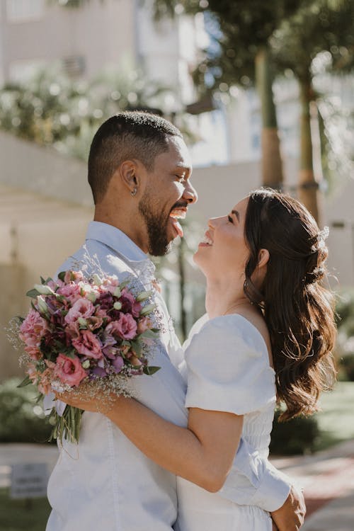 A bride and groom are smiling and holding flowers