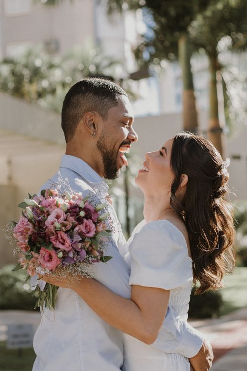 Free Happy couple embracing outside on a sunny day, holding a bouquet of flowers. Stock Photo