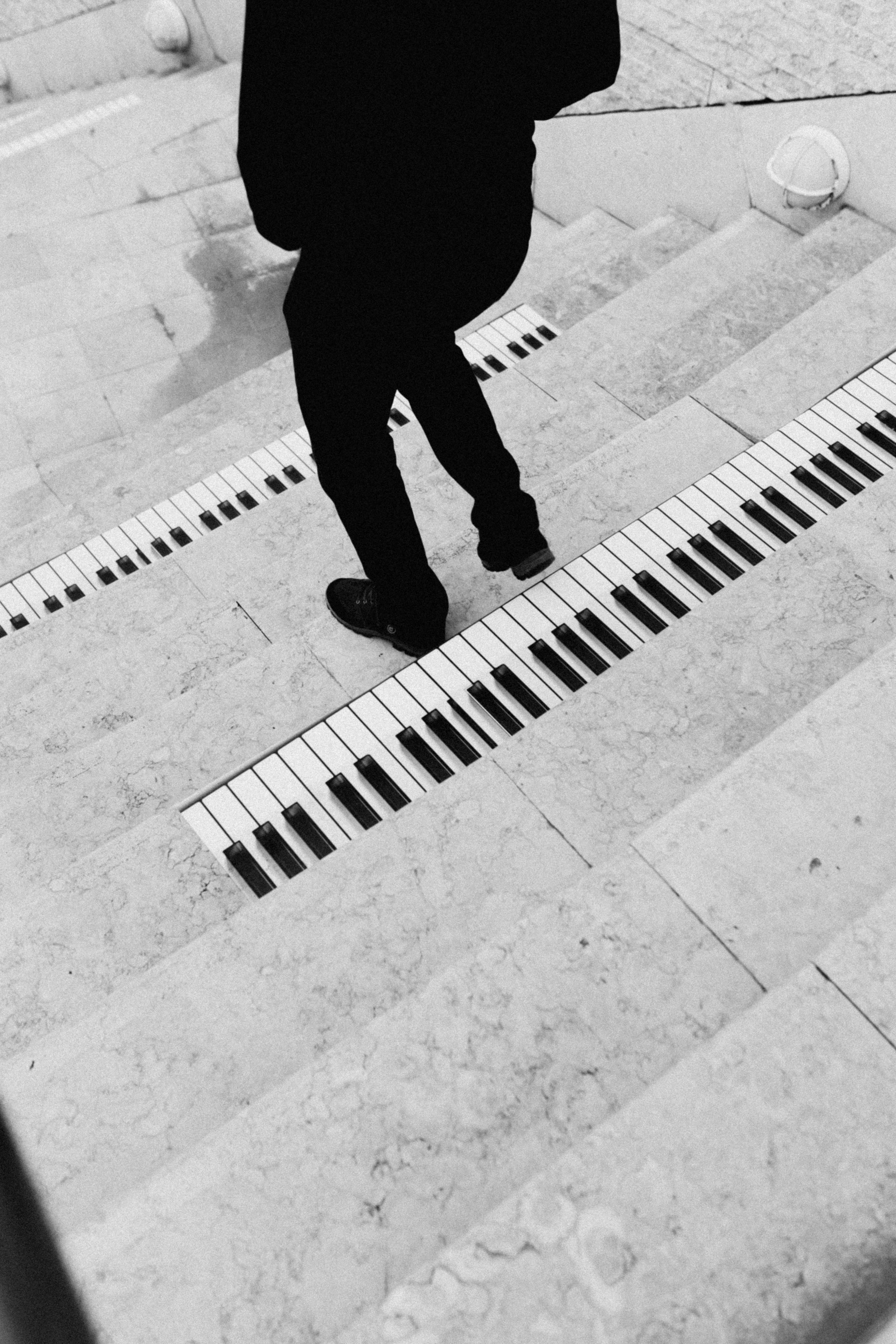 Black and white photo of piano keys painted on city stairs, featuring a man walking down.