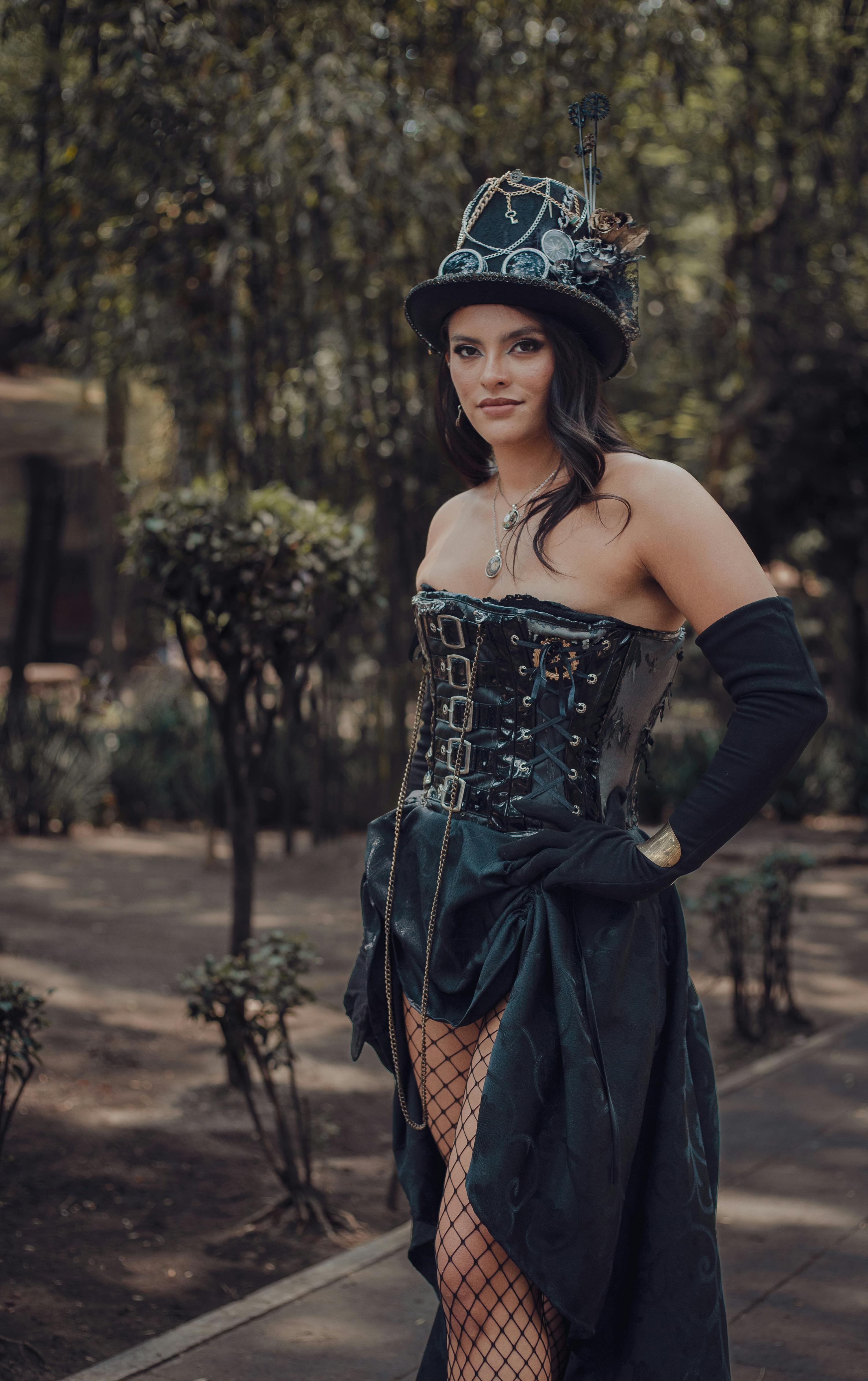 Elegant woman in steampunk cosplay with corset and hat, posing outdoors.
