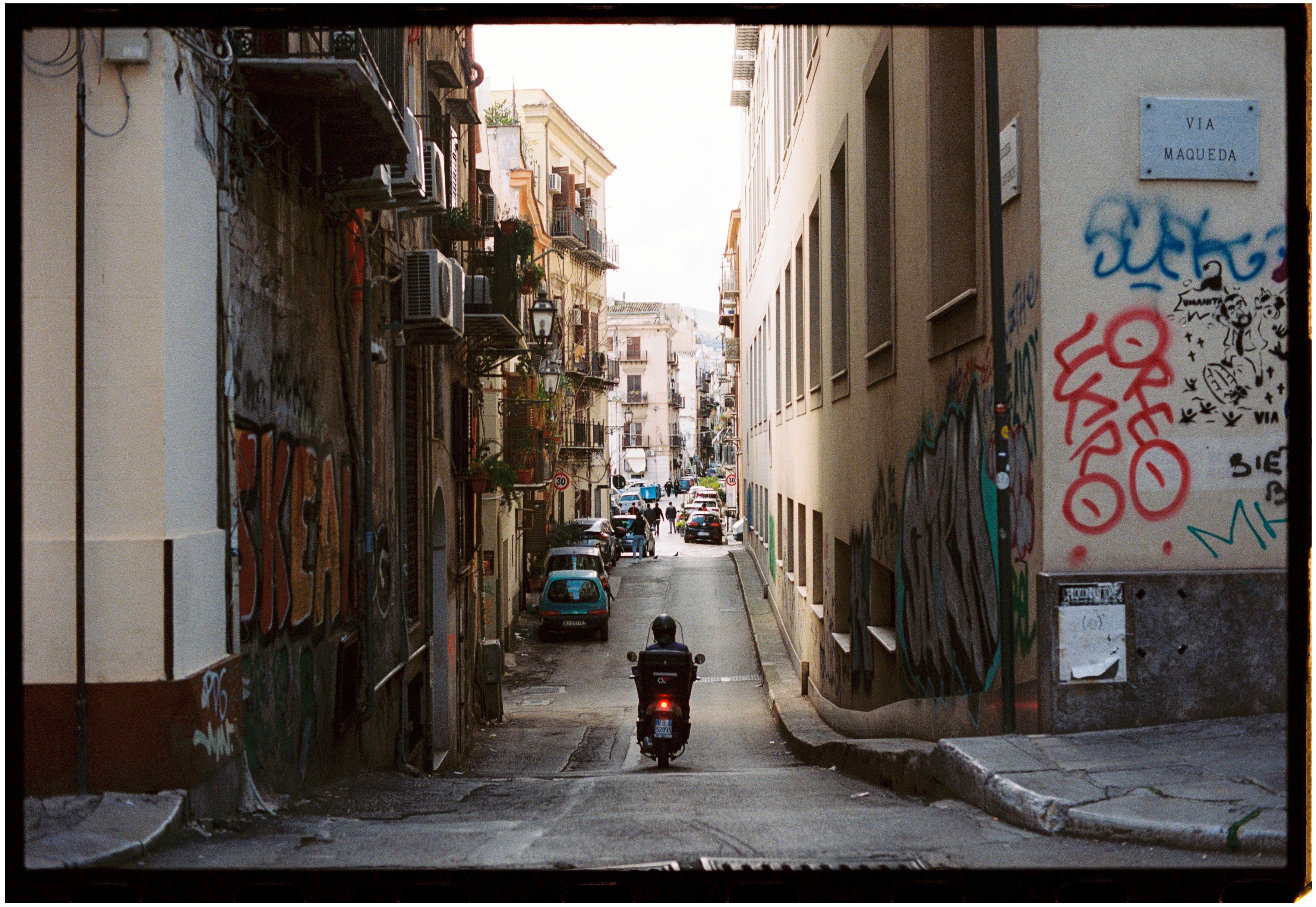 A classic street view in Palermo with vibrant graffiti and a scooter rider.