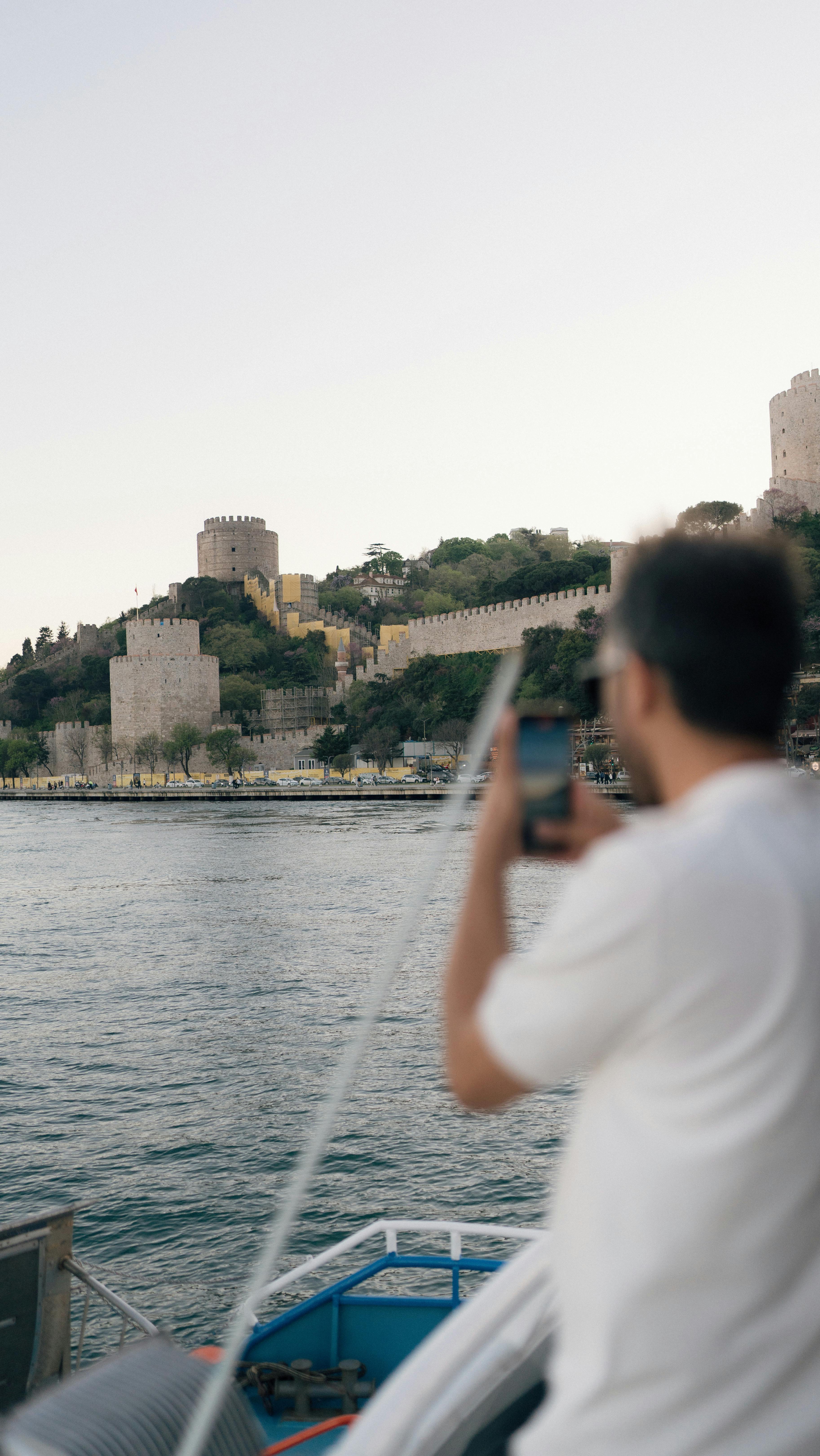 man standing on a boat taking pictures of the rumelihisari castle in istanbul turkey
