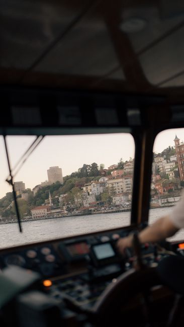 Fotomural Interior de un cockpit de barco con vista a un pueblo costero, mostrando elementos de navegación y vela.