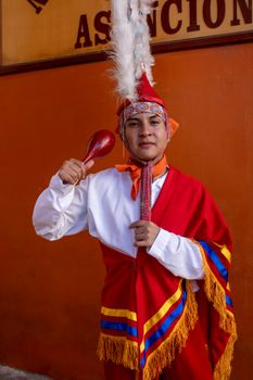 Traditional dancer in colorful Mexican attire holding a maraca against an orange wall. — photo by Omar Tapia