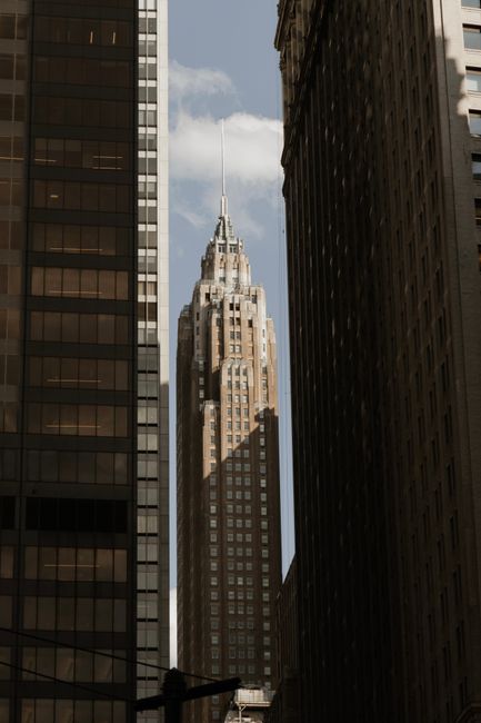 A stunning view of an Art Deco skyscraper framed by Manhattan buildings under a clear sky.