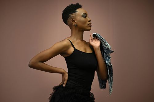 Free Profile view of a woman in a black dress posing gracefully with a denim jacket in a studio. Stock Photo