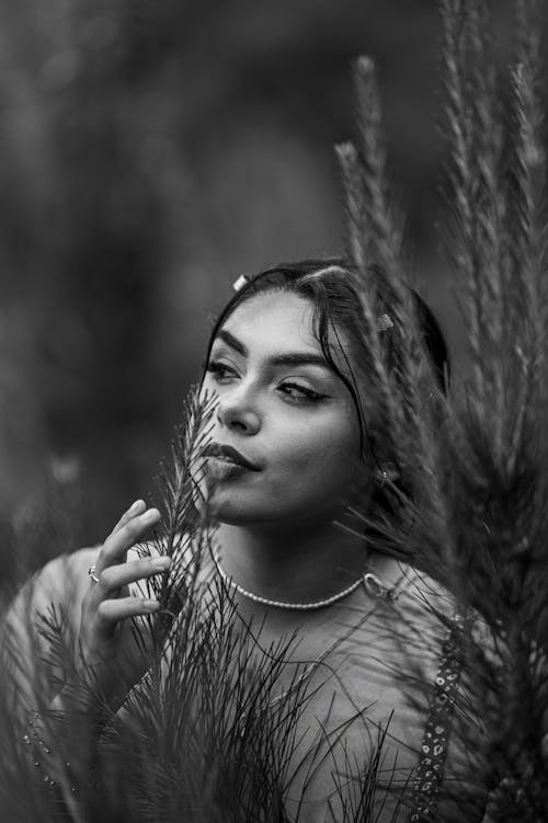 Black and White Photo of a Young Woman Posing Outside between Plants