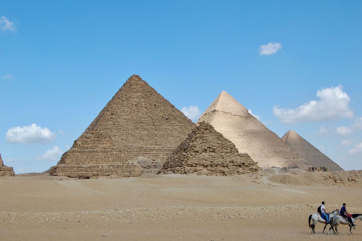 Horses and riders in the desert in front of the pyramids of Giza, Egypt