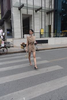 Fashionable woman in modern outfit walking confidently across a city crosswalk. Urban lifestyle captured in daylight.