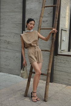 Fashionable woman in neutral tones poses by ladder, showcasing modern style.