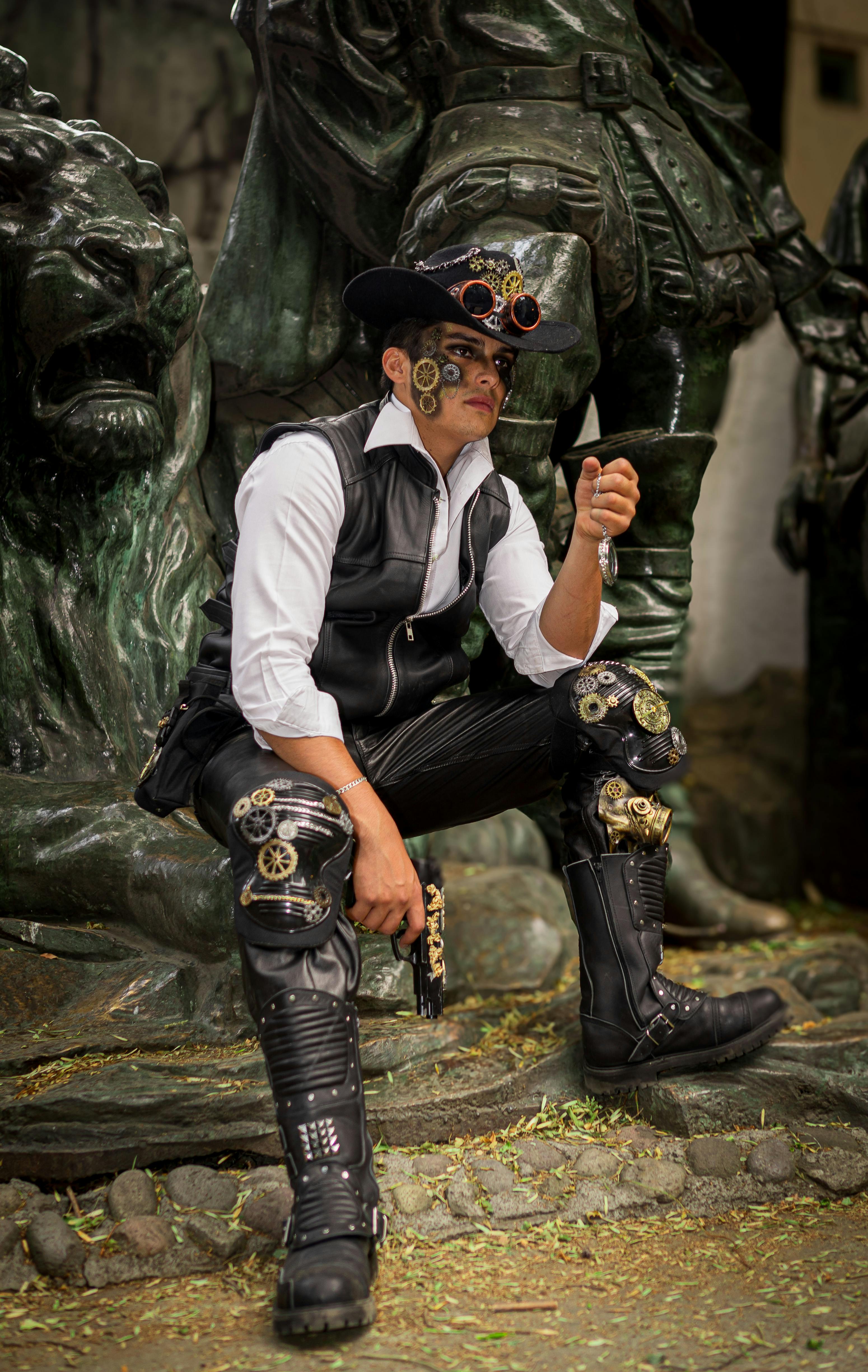 A man in steampunk fashion poses next to statues, embodying a unique style.