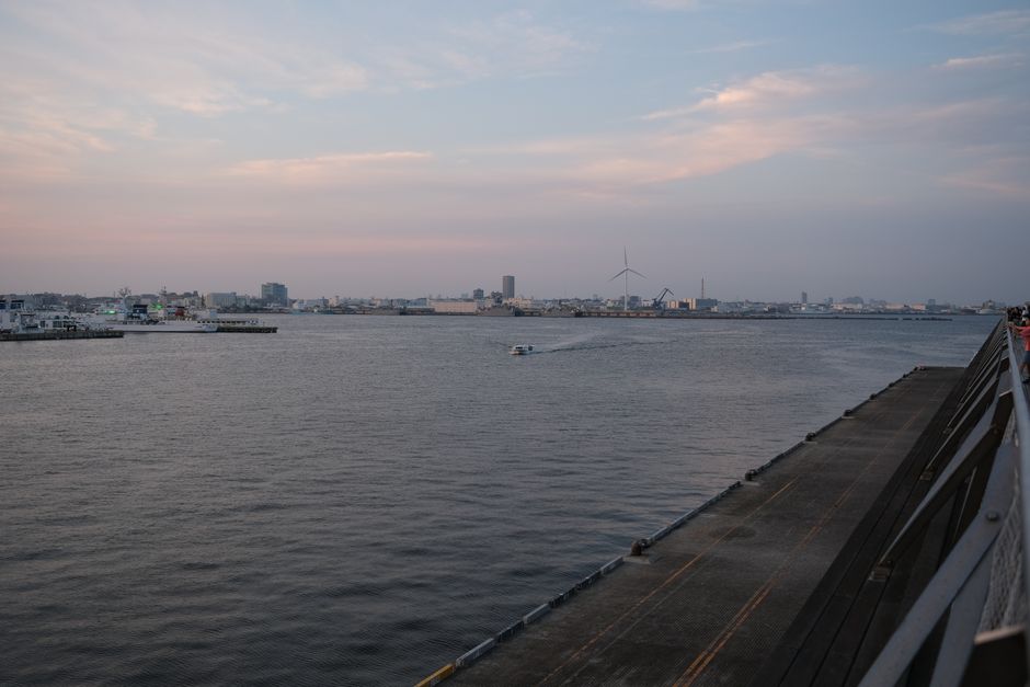 Tranquil view of a motorboat on Yokohama bay with city skyline at dusk.
