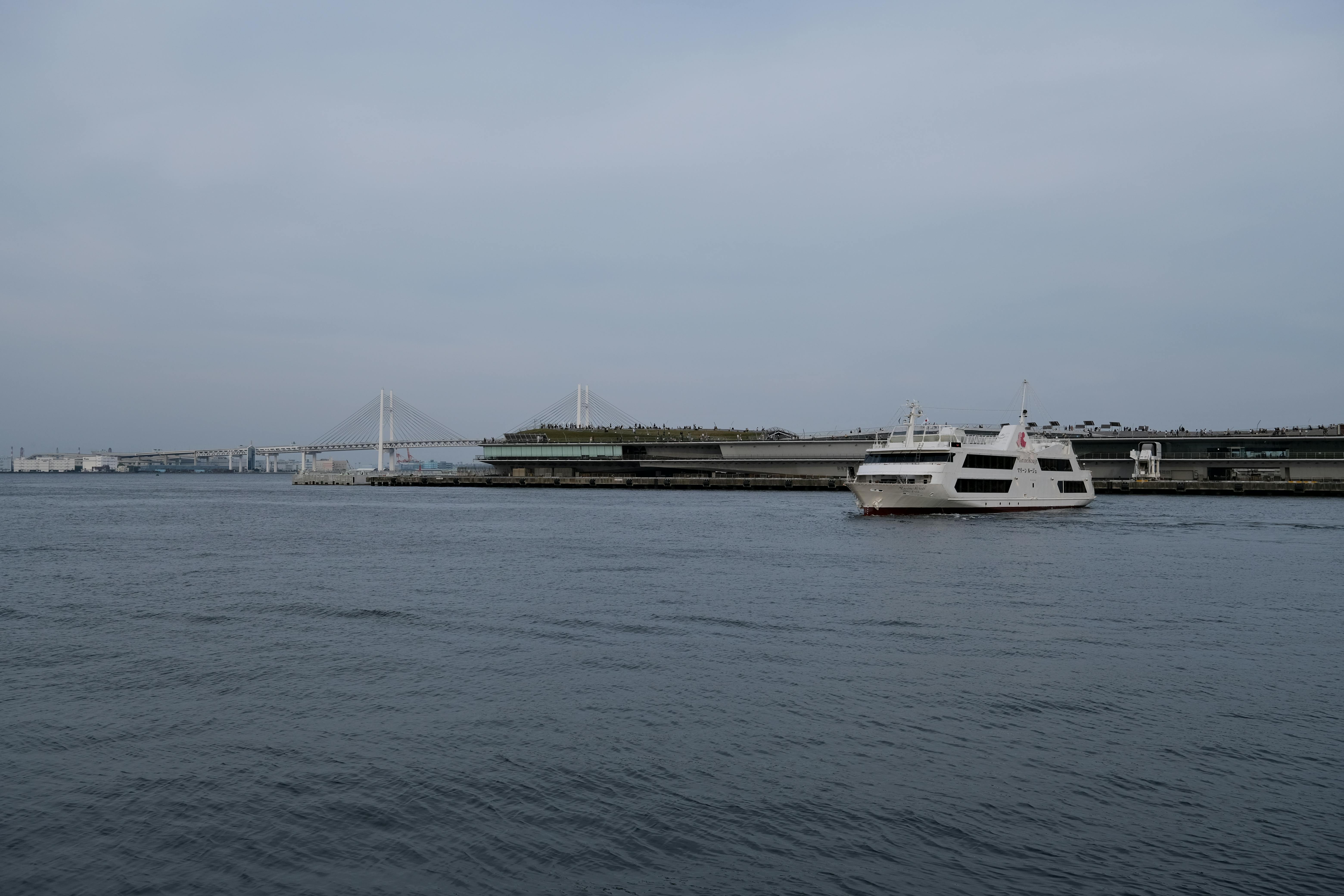 White ferry cruising near Yokohama Bay Bridge in calm waters, ideal for travel enthusiasts.