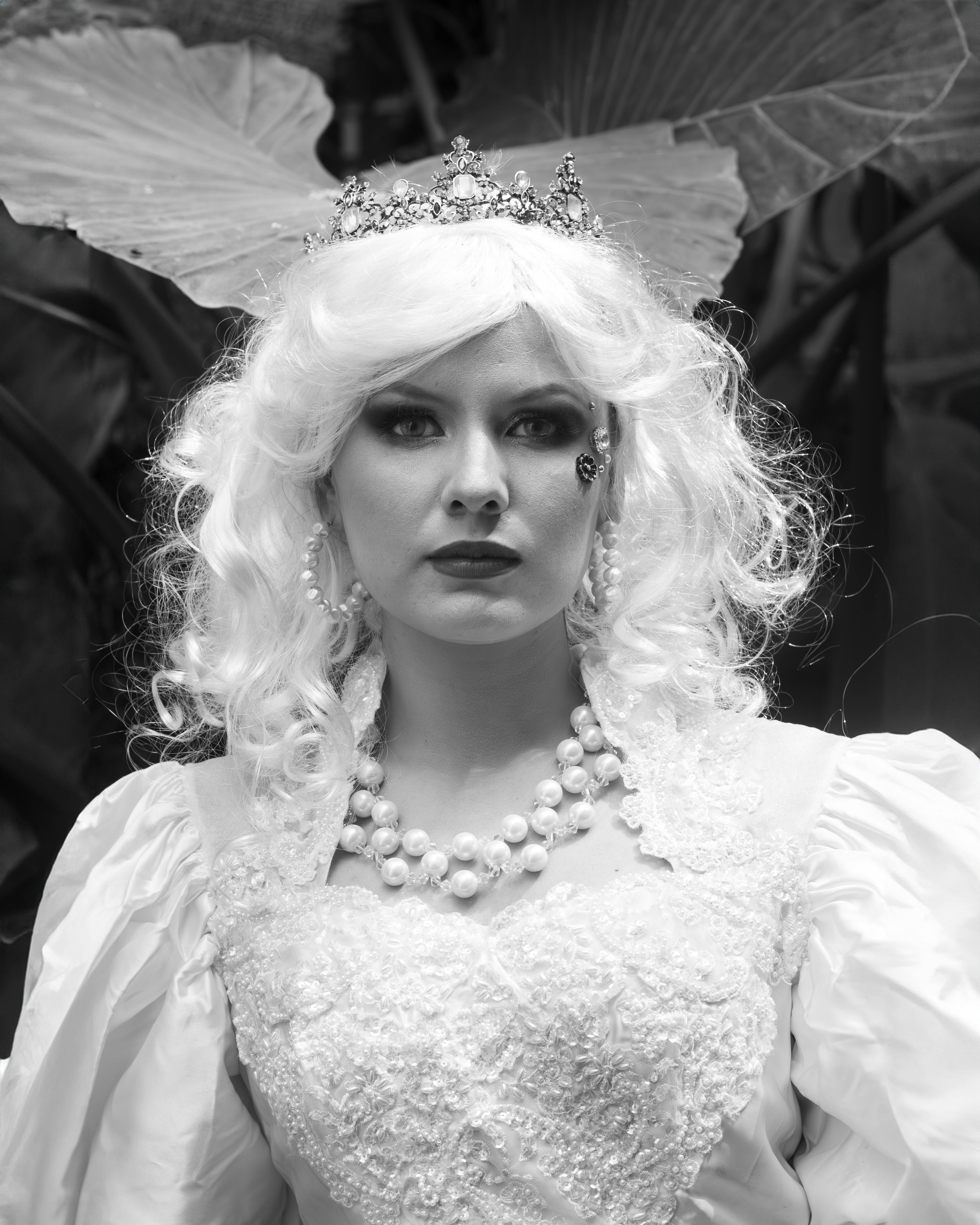 Black and white portrait of a woman in an elaborate costume with a crown, pearls, and white wig.