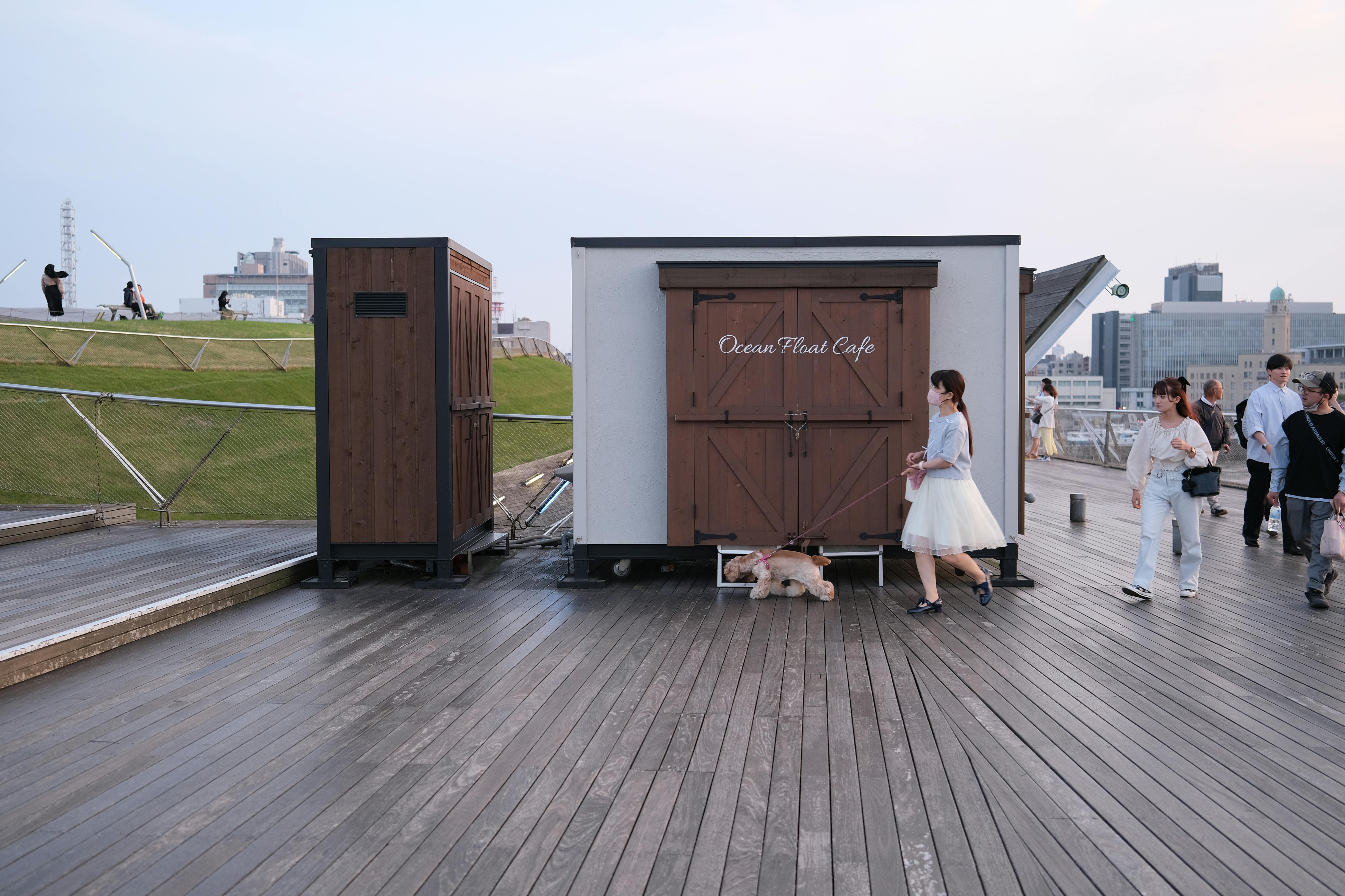 People and pets walking by Ocean Float Cafe in Yokohama's promenade.