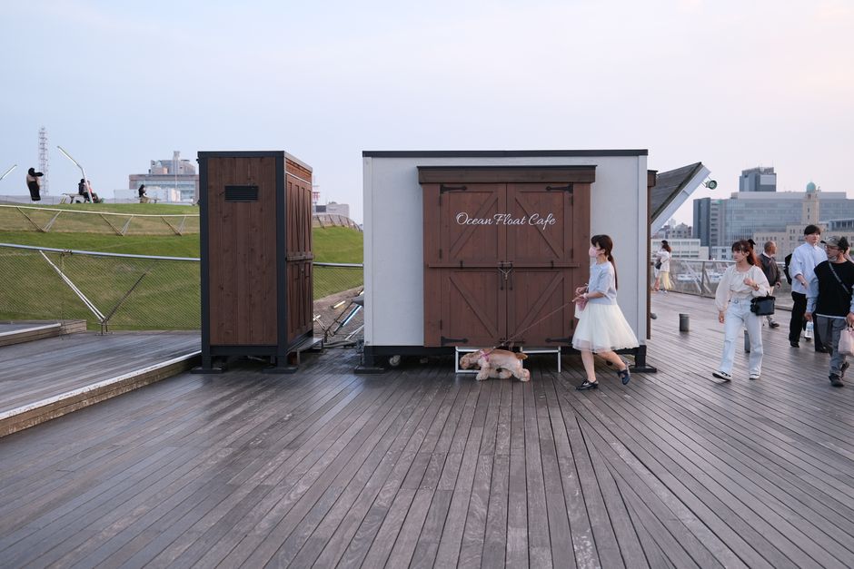 People and pets walking by Ocean Float Cafe in Yokohama's promenade.