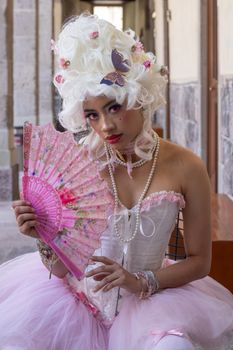 A woman in a vintage costume with pearls and a decorative pink fan, exuding elegance and historical flair.