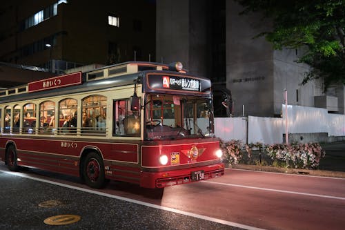 A red and white bus driving down a street at night