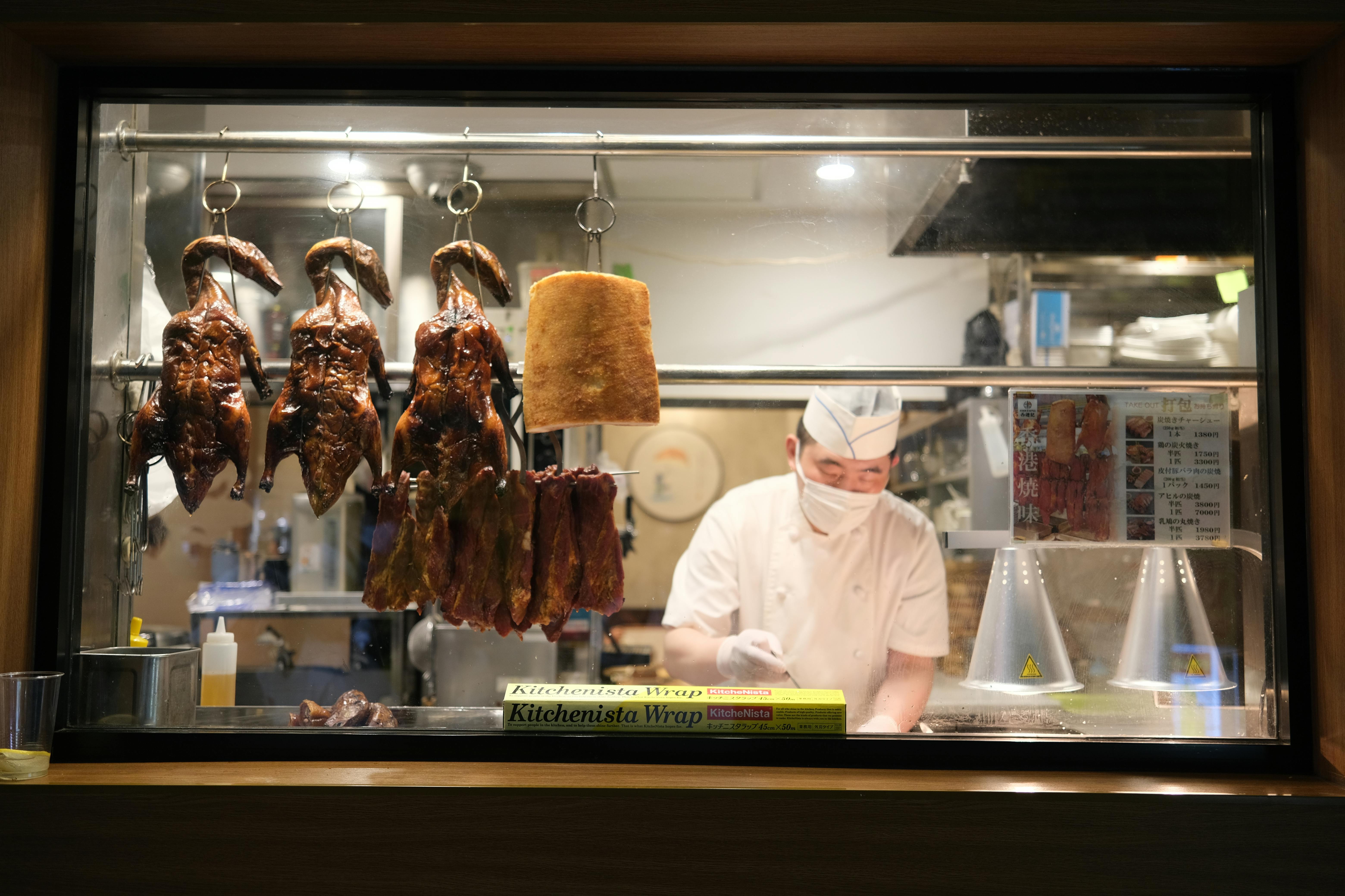 Chef in restaurant kitchen preparing roast duck and meat cuts, Yokohama, Japan.
