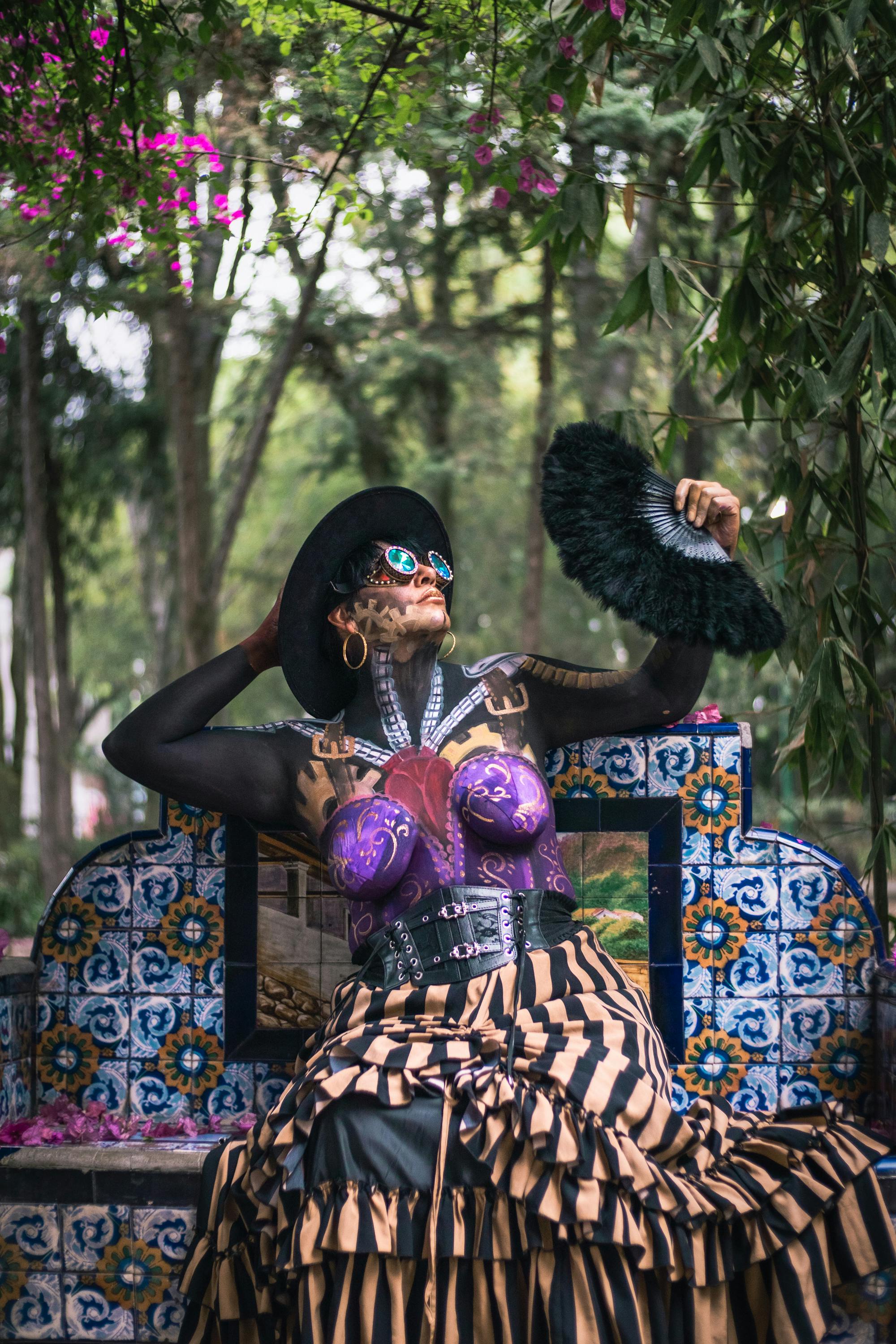 Eccentric steampunk woman posing outdoors in vibrant attire with fan.