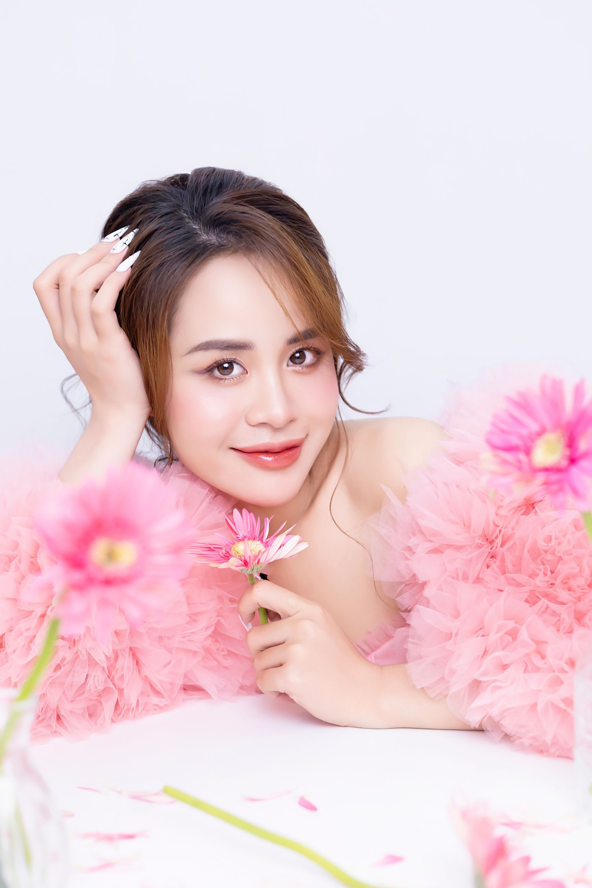 Close-up portrait of a young woman with pink flowers against a white backdrop.