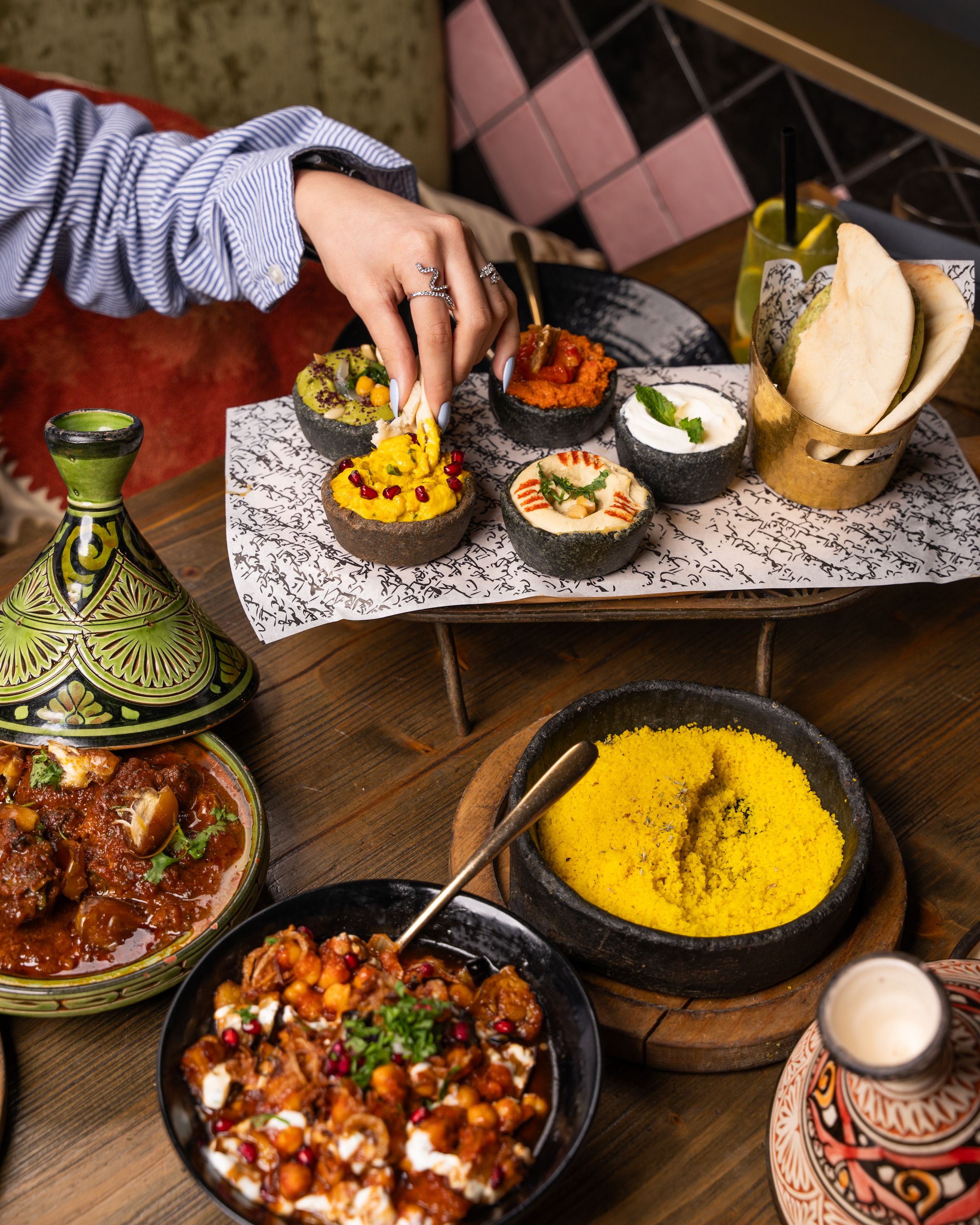 Table en bois garnie : tajine ouvert, bols de purées et de houmous, corbeille de pain plat et grand bol de semoule jaune safranée