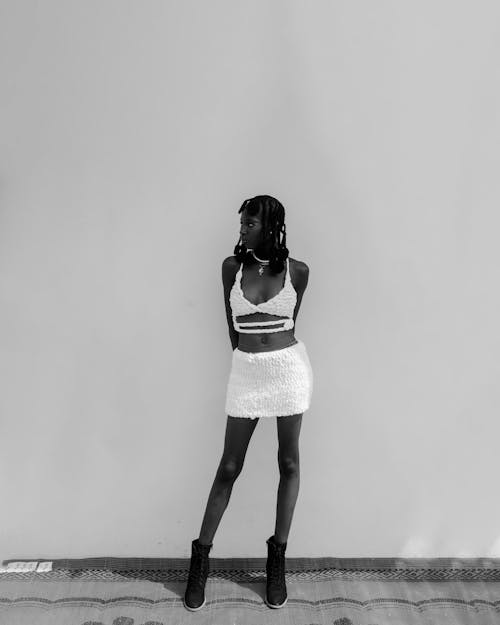 A woman in a white skirt and boots standing in front of a wall