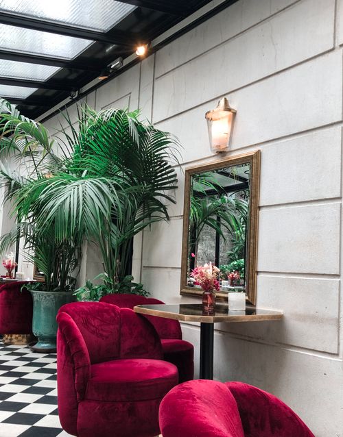 Free Stylish Parisian interior featuring red velvet chairs, tropical plants, and a classic mirror. Stock Photo