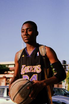 A confident young basketball player holding a ball during daytime outdoor shoot.