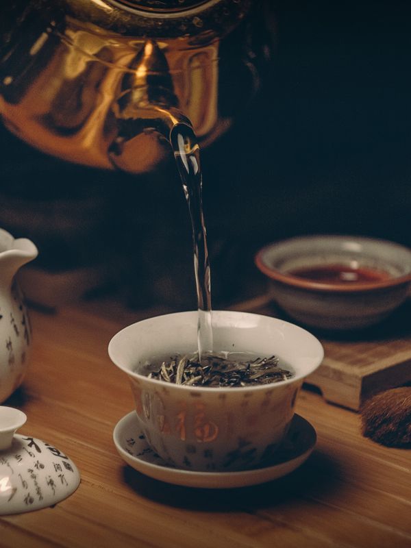 A pale porcelain cup of golden tea with a faint wisp of steam, beside a small pot.