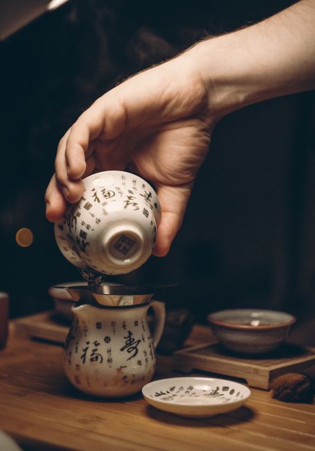 A hand skillfully pours tea in a traditional Chinese teacup during a cozy indoor tea ceremony.