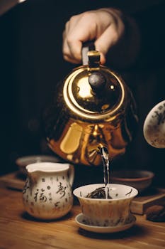 Close-up of a golden teapot pouring tea into a cup with Chinese calligraphy.