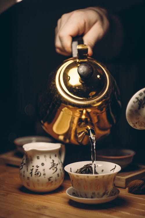 Free Person Holding Gold Teapot Pouring White Ceramic Teacup Stock Photo