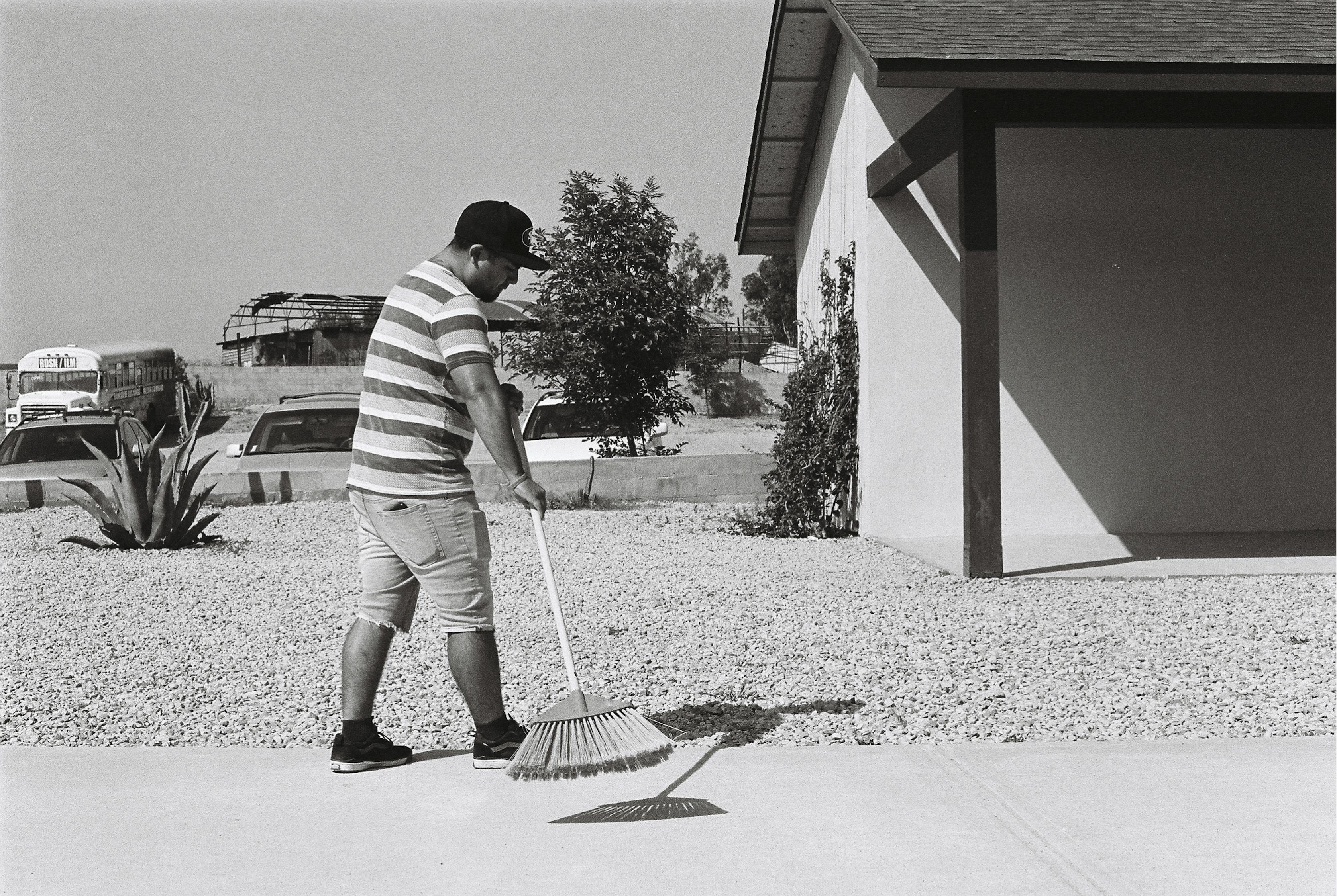 Grayscale Photo of Man Sweeping Driveway