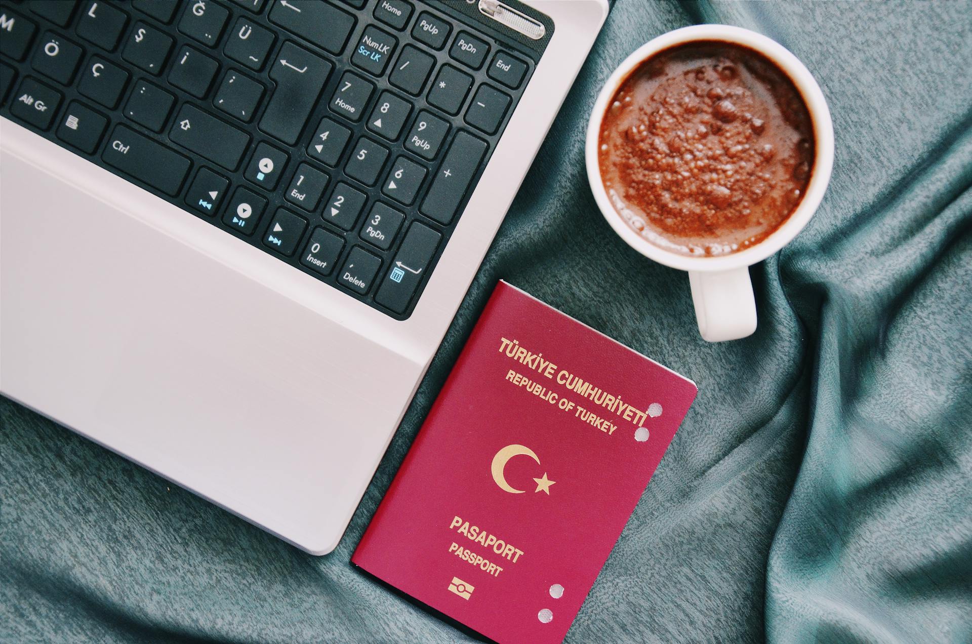 A Turkish passport beside a coffee cup and laptop, symbolizing travel and technology.