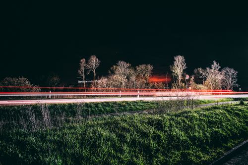Free Long exposure of light streaks on a rural road at night, surrounded by trees and grass. Stock Photo