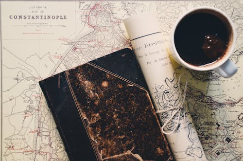 두루마리 종이와 두꺼운 표지의 책 근처 머그잔에있는 블랙 커피