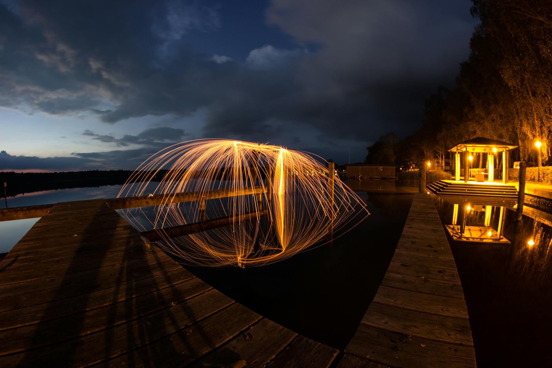 Stunning long exposure of fiery light art over a tranquil lakeside pier at dusk.