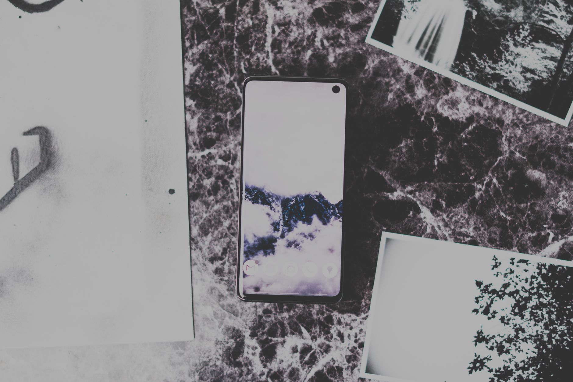 Flat lay of a smartphone on marble surface surrounded by black and white photos, creating a modern and artistic vibe.