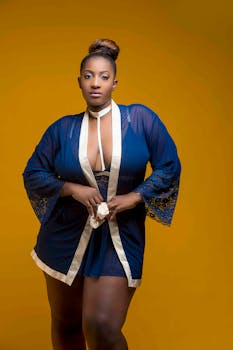 一位身着蓝色长袍的女性，以自信的姿态立于鲜明的黄色背景前，构成了一幅时尚肖像