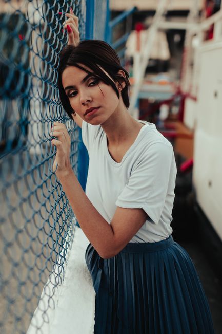 Elegant woman with short hair leaning against a blue fence, showcasing casual fashion.
