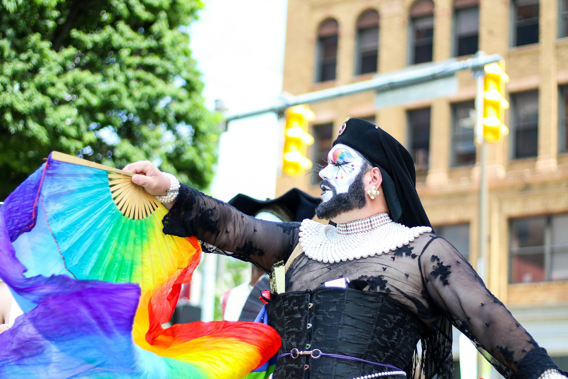 Colorful drag performer with rainbow flag celebrating at Pride Parade outdoors.